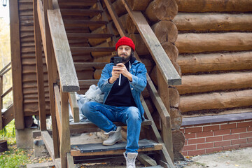man with a hipster beard in a red knitted hat and a denim jacket is sitting on the stairs