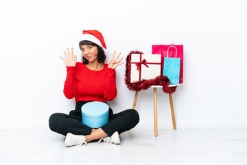 Young girl celebrating Christmas sitting on the floor isolated on white bakcground counting nine...