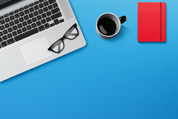 Modern workplace with laptop, coffee and notepad on blue background