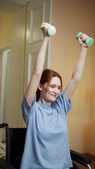 Fototapeta na wymiar A disabled woman is making hand exercises with dumbbells