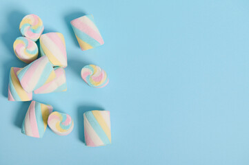 Flat lay minimalistic composition of colorful sweet marshmallows in the corner of a blue pastel background with copy space for advertising.