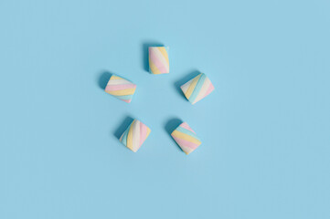 Flat lay food composition of colorful multi colored sweet sugary marshmallows laid out in the shape of five-pointed star on blue pastel colored background with copy space for advertising