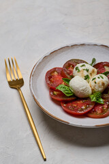 Vertical view caprese salad with red tomatoes, basil and mozzarella cheese in white plate and golden fork