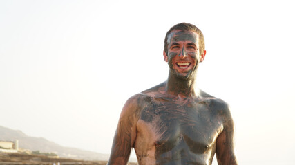 Male tourist rubbed in mud at the Dead Sea in Jordan.