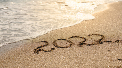 The concept of waiting for the new year and new life. The inscription Evening 2022 against the backdrop of bright sunlight and sea waves.