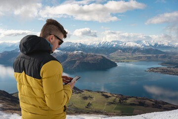 Man with using smartphone in mountain summit. Roy's Peak, Wanaka, New Zealand