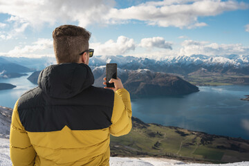 Caucasian man taking picture with mobile at Southerns Alps in Roy's Peak Summit Wanaka, New Zealand