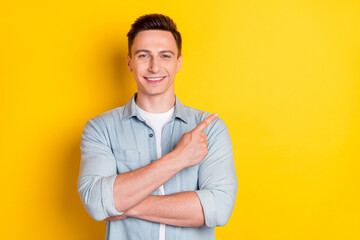 Portrait of attractive cheerful guy demonstrating copy empty space ad isolated over bright yellow...