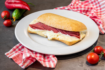 Salami and cheddar sandwich on white porcelain plate on stone table