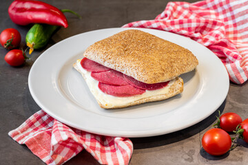 Salami and cheddar sandwich on white porcelain plate on stone table