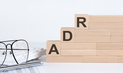 wooden cubes with letters ADR on the white table with keyboard and glasses