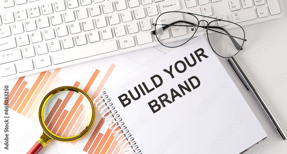 Poster build your brand text written on notebook with keyboard, chart,and glasses