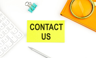Sticker with the text CONTACT US on a white background, near calculator and notebook