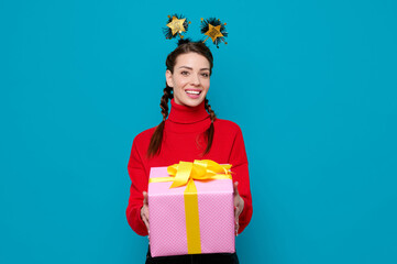 Happy smiling woman in red sweater celebrate new year party holds gift box on blue isolated background.
