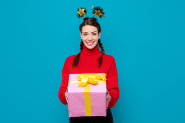 Happy smiling woman in red sweater celebrate new year party holds gift box on blue isolated background.