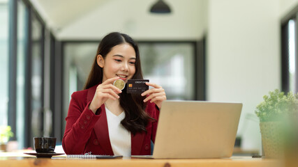 Happy businesswoman holding bitcoin token and credit card in office