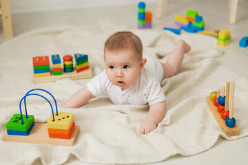 cute baby is lying on his stomach on a gray linen blanket and playing with colored educational toys. products for children. concept of a happy childhood and motherhood. child care. space for text