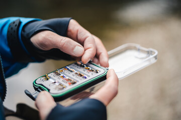 Fly fisherman chooses artificial flies from lures box for fly fishing at river. Blurry close up. © Patrik