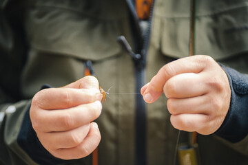 Close up of young fisherman's hands tying a Fly Fishing Knot. Fly fishing concept. - obrazy, fototapety, plakaty