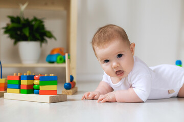 Naklejka premium cute baby is lying on his stomach on a gray linen blanket and playing with colored educational toys. products for children. concept of a happy childhood and motherhood. child care. space for text