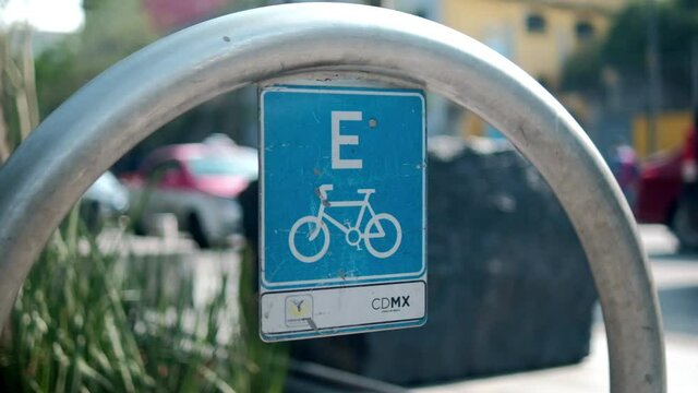Blue bicycle parking spot sign on metal arch with traffic as background