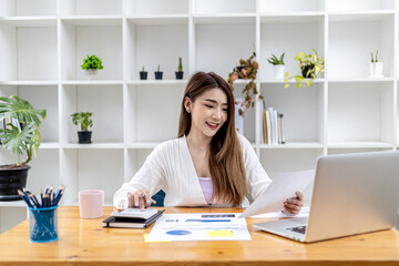 Beautiful Asian businesswoman sitting in her private office, chatting with her partner via laptop and checking documents, she is a female executive of a startup company. Financial management concept.