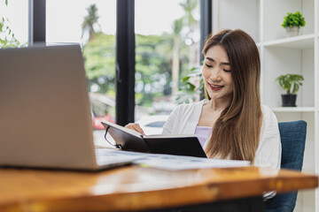 A beautiful Asian businesswoman working in the room, she is writing her schedule to remind herself in her notebook, she is a female executive of a startup company. Concept of financial management.