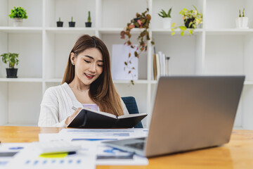 A beautiful Asian businesswoman working in the room, she is writing her schedule to remind herself in her notebook, she is a female executive of a startup company. Concept of financial management.
