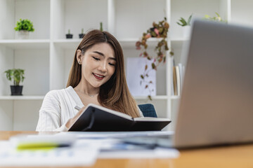 A beautiful Asian businesswoman working in the room, she is writing her schedule to remind herself in her notebook, she is a female executive of a startup company. Concept of financial management.
