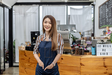 Fototapeta na wymiar Portrait of a beautiful Asian woman in an apron standing in a coffee shop, she owns a coffee shop, the concept of a food and beverage business. Store management by a business woman.