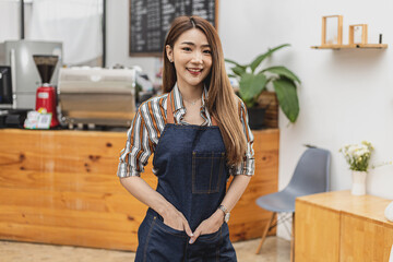 Portrait of a beautiful Asian woman in an apron standing in a coffee shop, she owns a coffee shop, the concept of a food and beverage business. Store management by a business woman.