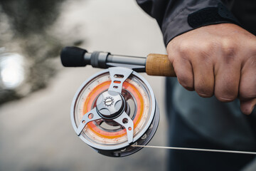 Closeup of fly-fisherman using rod with reel in river.