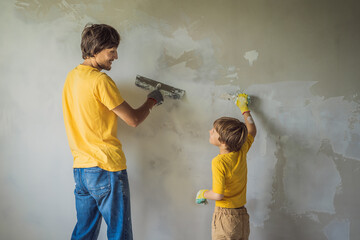 Man with his son makes repairs at home, he teaches children to plaster the walls with a spatula in...
