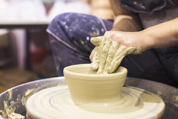 Pottery artist hands molding clay vase on pottery wheel at art workshop.