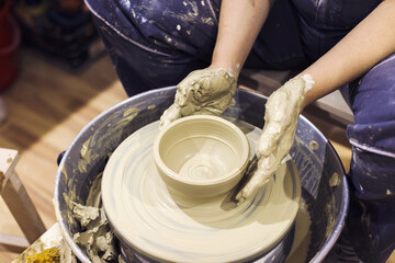 Pottery artist hands molding clay vase on pottery wheel at art workshop.