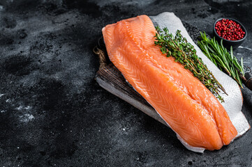 Fresh raw salmon fillet fish on cutting board with knife. Black background. Top view. Copy space