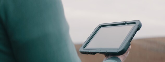CU on hands, Caucasian male farmer using a tablet while standing in the field. Cloud technology for agriculture. Shot with 2x anamorphic lens