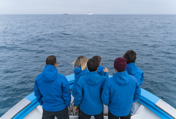 Crew members in blue uniforms standing on a boat dividing the sea and other boats.