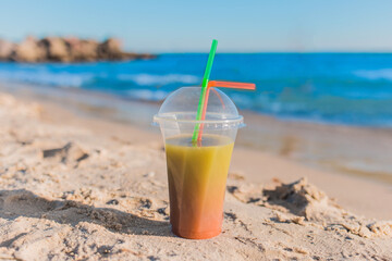Colored chilled non-alcoholic cocktail stands on the sand of the sea beach against the background of water and sky