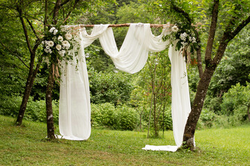 Outside wedding ceremony. Very beautiful and stylish wedding arch, decorated with various fresh flowers, standing in the garden.
