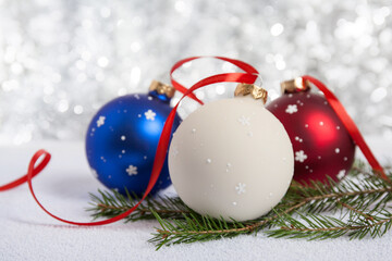 Christmas decoration - hand-painted Christmas balls in white, blue and red colors. Blurred background of silver color. Fir branches. Red ribbon. Suitable for making any New Year and Christmas design