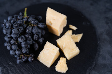 Pieces of aromatic parmesan and black raisins grapes on a dark background. Wine plate.