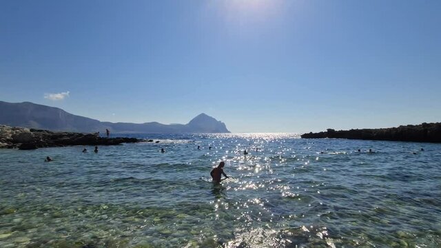 Sun reflections over sea water and people bathing at Baia Santa Margherita in southern coast of Italy in Sicily