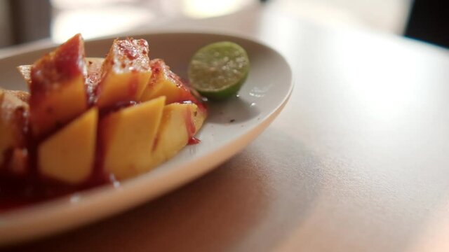 Plate of chopped mango with Mexican chamoy sauce and blurry background