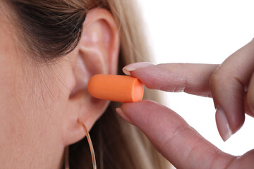 Woman inserts orange earplugs into ears closeup