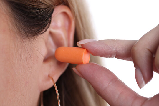 Woman inserts orange earplugs into ears closeup