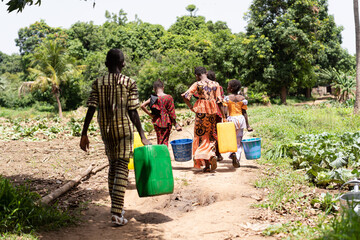 Group of tired black African school-age children busy carrying water back and forth from the...