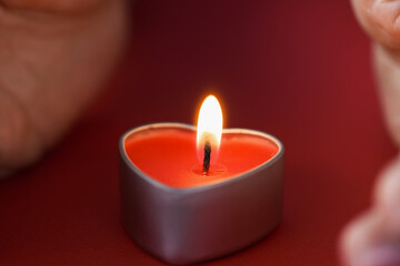 Female hands holding a heart shaped candle in dark closeup
