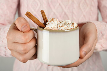 Woman holding cup of delicious hot chocolate with marshmallows and cinnamon sticks, closeup