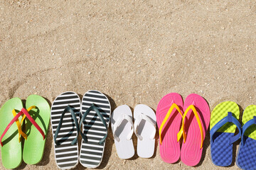 Many different flip flops on sand, flat lay. Space for text